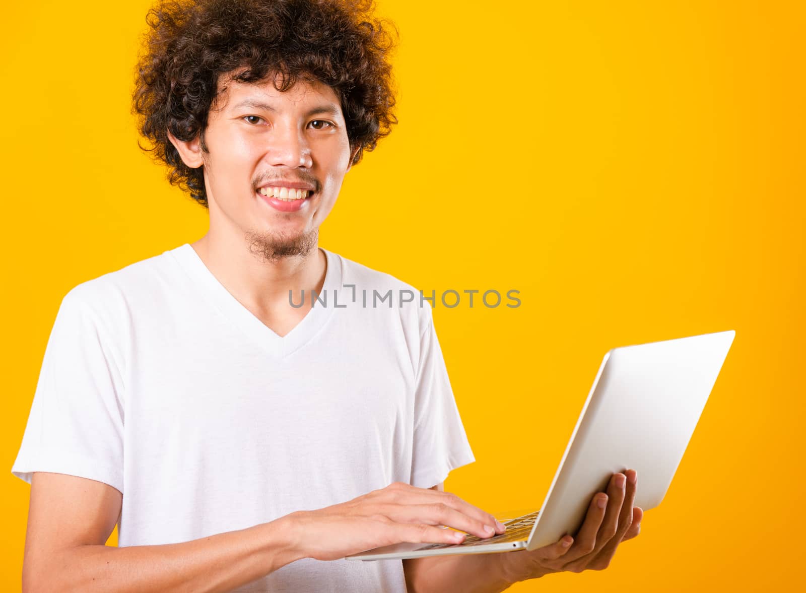 Asian handsome man with curly hair using laptop computer isolate on yellow background with copy space for text