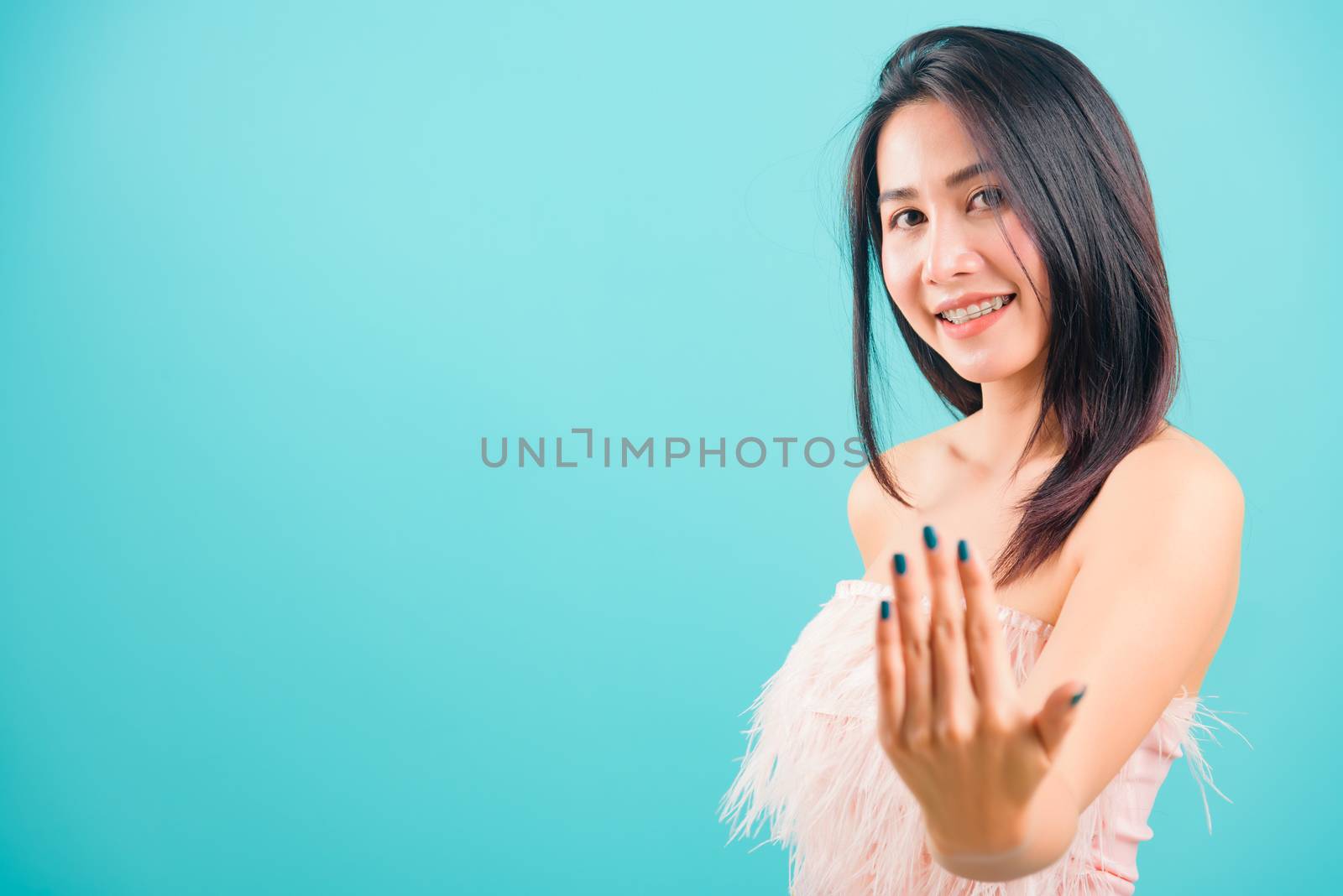 Smiling face Asian beautiful woman making gesture with hand inviting to come and her looking to camera on blue background, with copy space for text