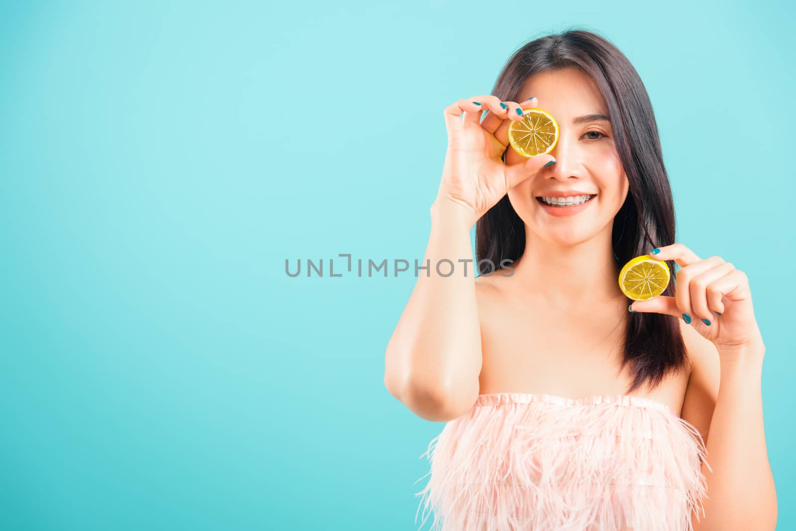 Portrait asian beautiful woman smiling her holding halves of orange on face near eyes on blue background, with copy space for text