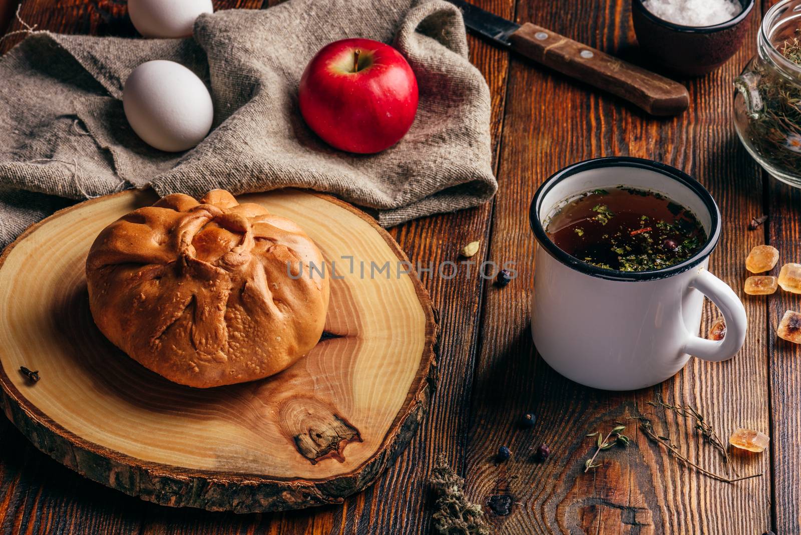 Rustic breakfast with traditional tatar pastry elesh, herbal tea in metal mug, apple and boiled eggs over dark wooden surface