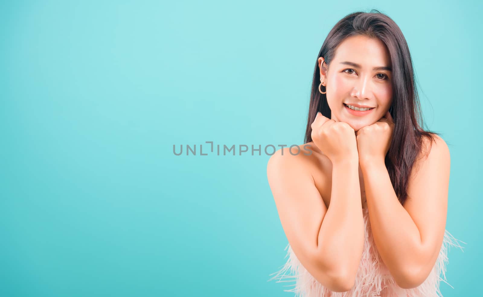 Smiling face Asian beautiful woman her glad keeps both hands under chin smiles pleasantly on blue background, with copy space for text