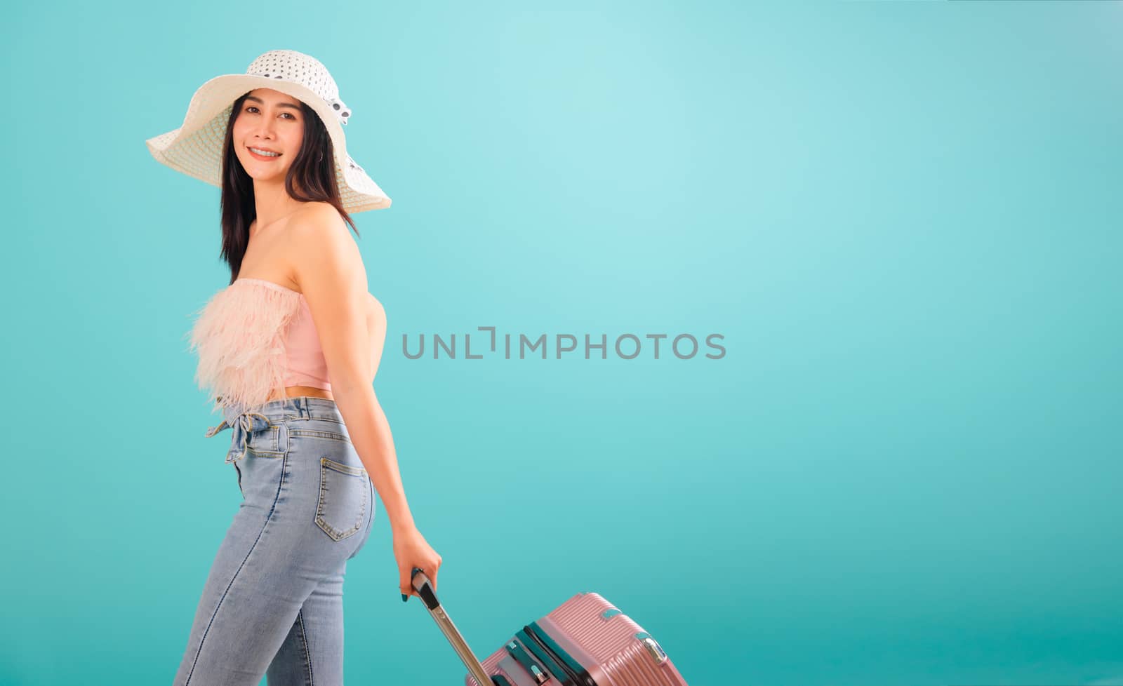 Portrait asian beautiful woman with hat her drag luggage or travel bag to travel weekends on blue background, with copy space for text