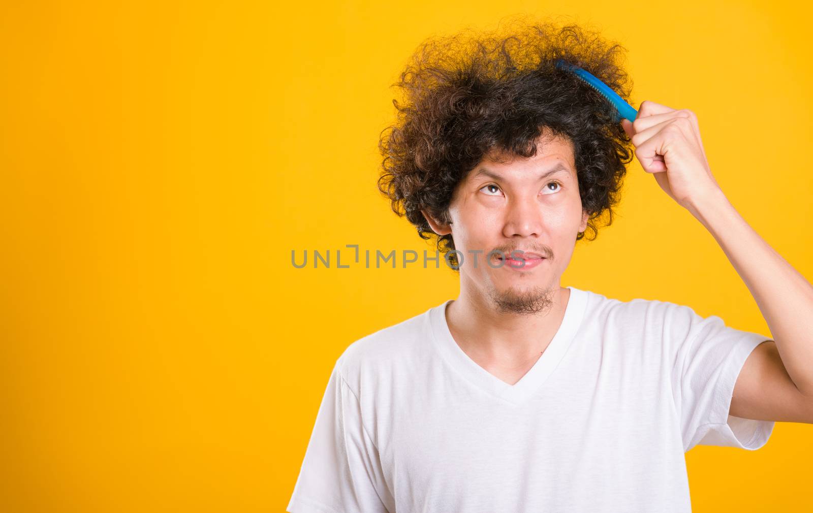 Asian man combing curly hair on yellow background by Sorapop