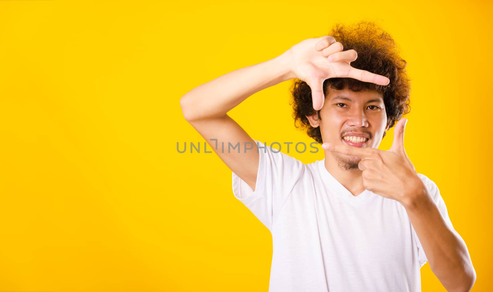 Asian handsome man with curly hair he smiling making frame with hands and fingers with happy face for creativity photography isolate on yellow background