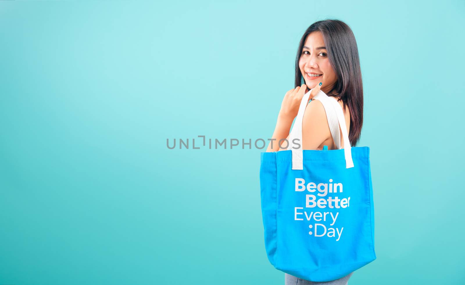 Smiling face portrait asian beautiful woman holding eco blue fabric bag on blue background, with copy space for text