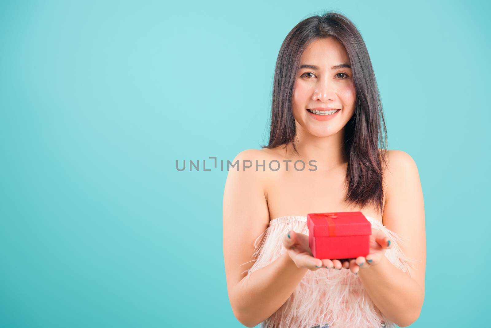 Portrait asian beautiful woman smiling her holding gift box and her 
looking to camera on blue background, with copy space for text