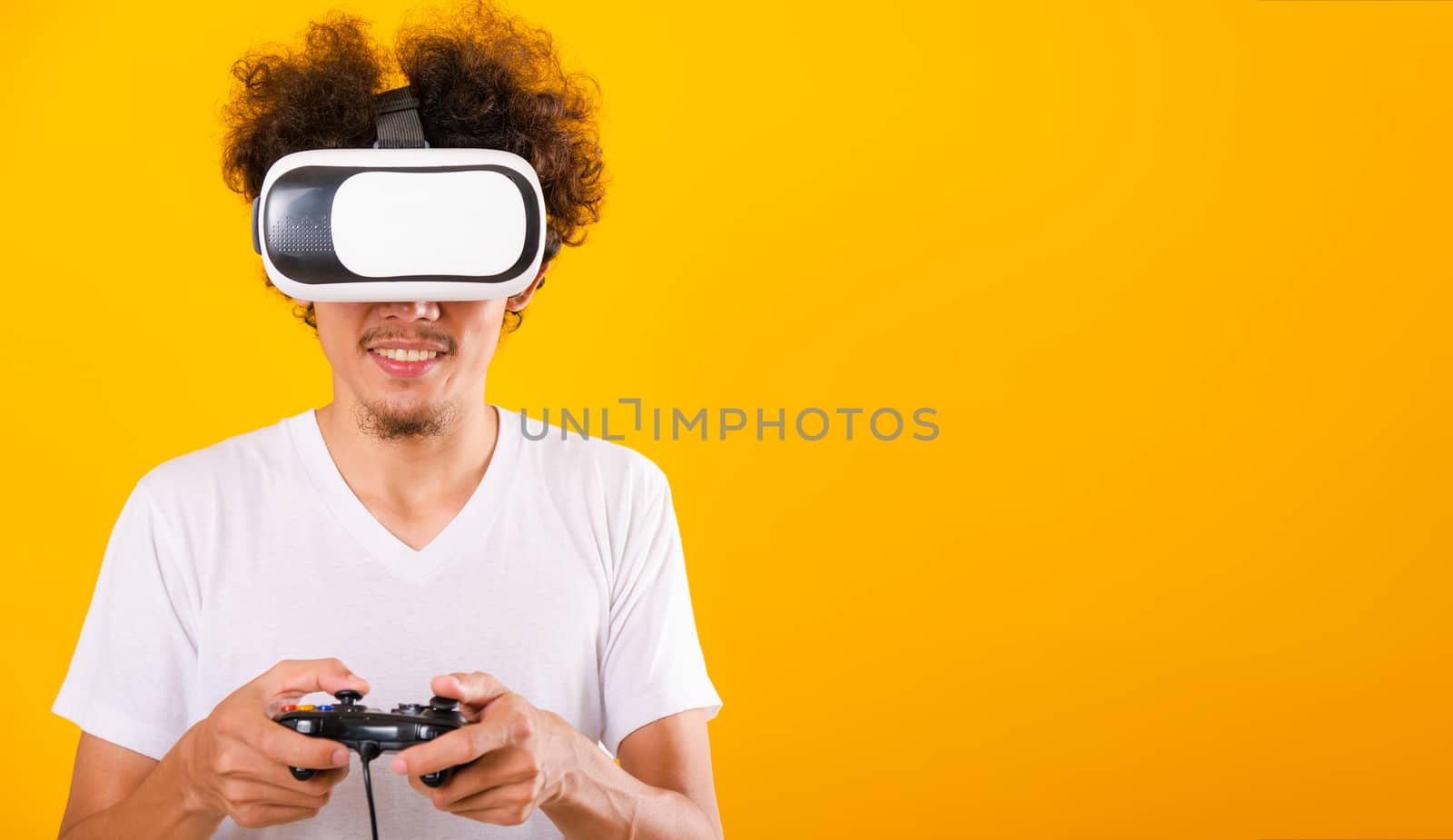 Asian handsome man with curly hair play game he using virtual reality headset or VR glass isolate on yellow background with copy space for text