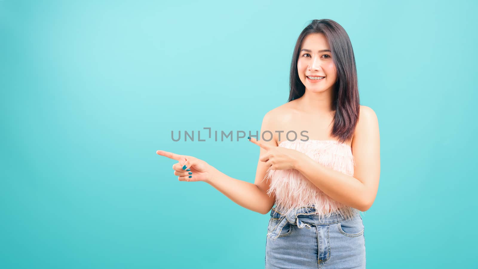 Portrait asian beautiful woman smiling looking camera her standing pointing finger out on blue background, with copy space for text