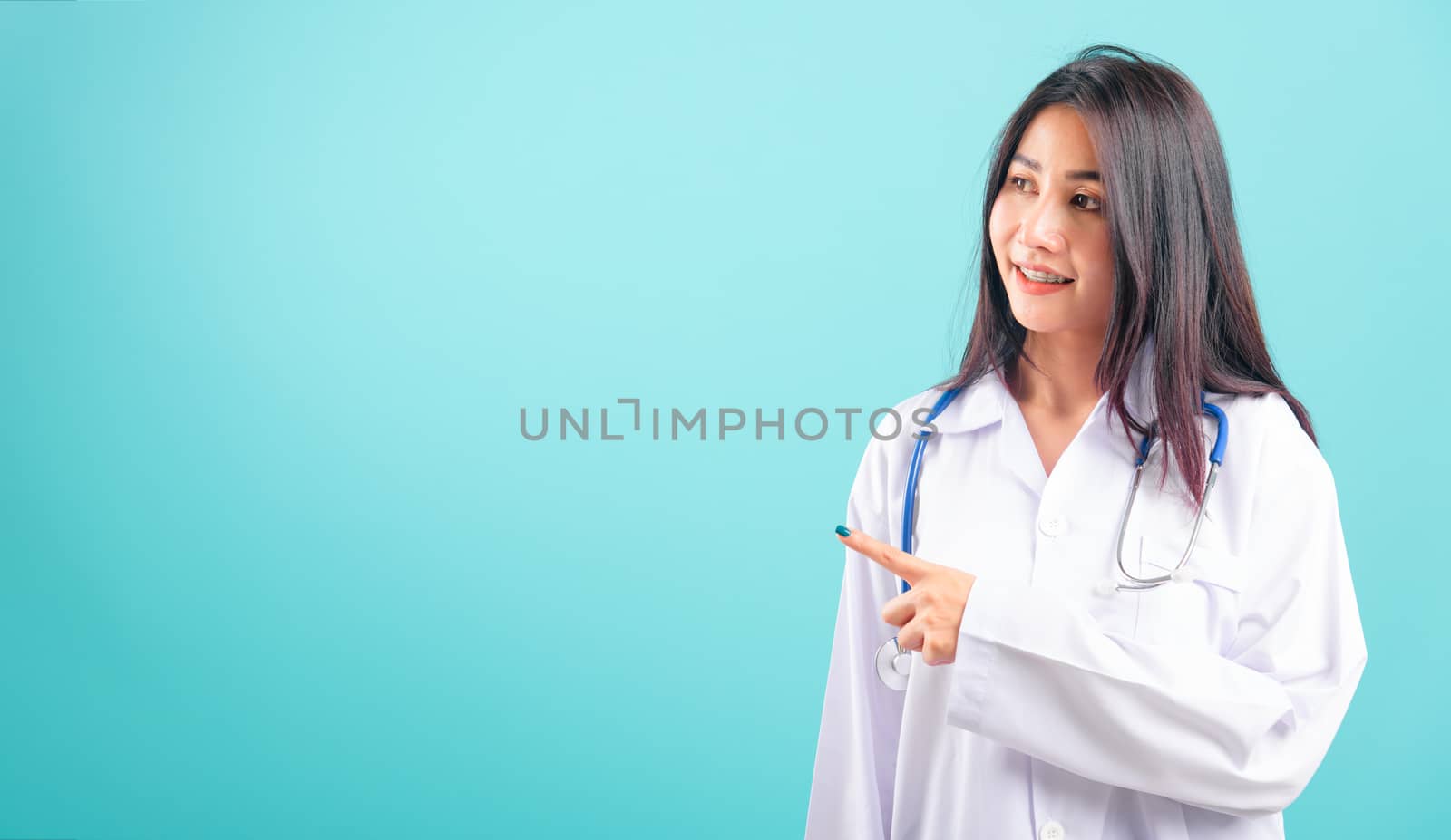 Portrait asian beautiful doctor woman smiling her standing pointing with finger on blue background, with copy space for text