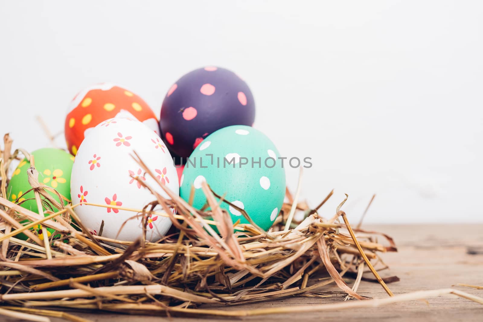 Beautiful Easter multi color egg in straw on wooden background, Easter day concept