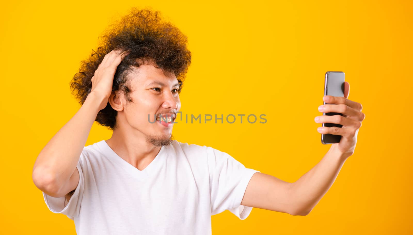 Portrait asian handsome man curly hair taking selfie with mobile phone isolated on yellow background