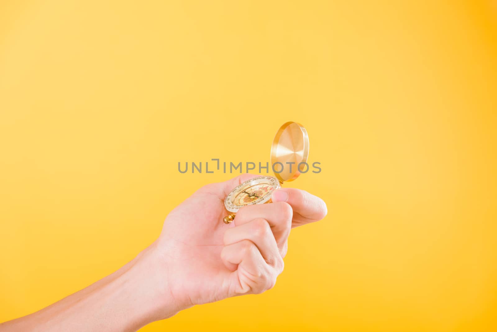 Hand holding antique brass compass isolated on yellow background with copy space for text