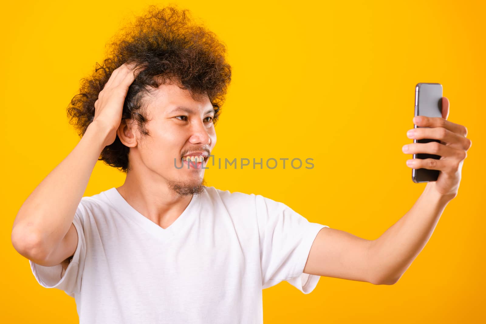 Portrait asian handsome man curly hair taking selfie with mobile phone isolated on yellow background