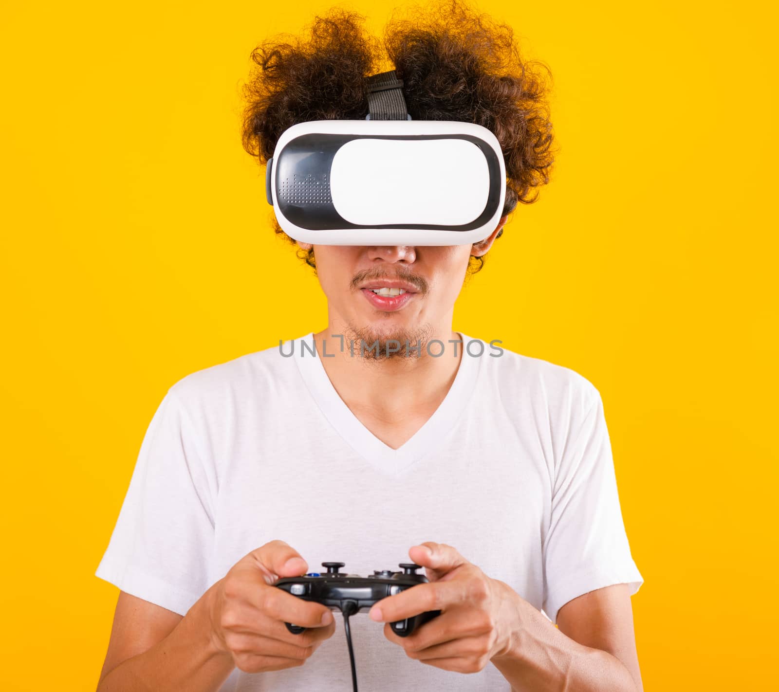 Asian handsome man with curly hair play game he using virtual reality headset or VR glass isolate on yellow background with copy space for text