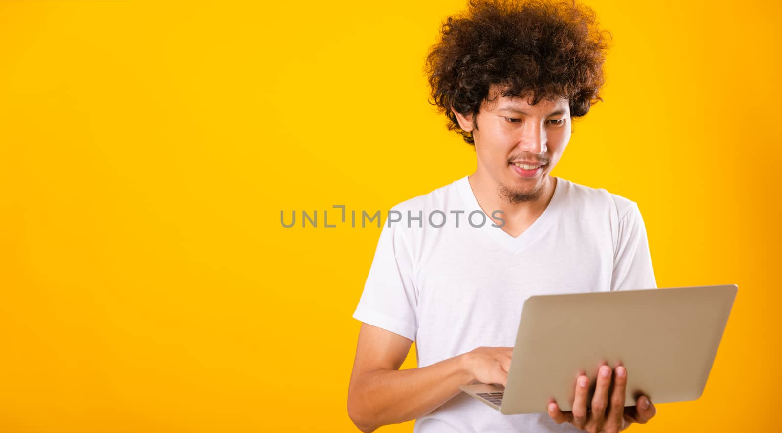 Asian handsome man with curly hair using laptop computer isolate on yellow background with copy space for text