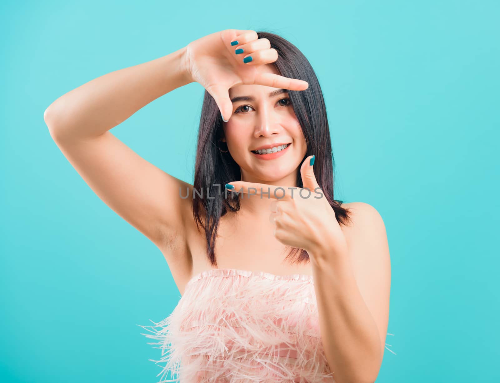 Smiling face asian beautiful woman her showing frame finger sign looking to camera on blue background, with copy space for text