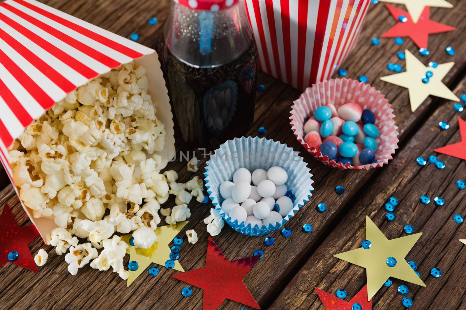 Scattered popcorn and sweet food decorated with 4th july theme on wooden table