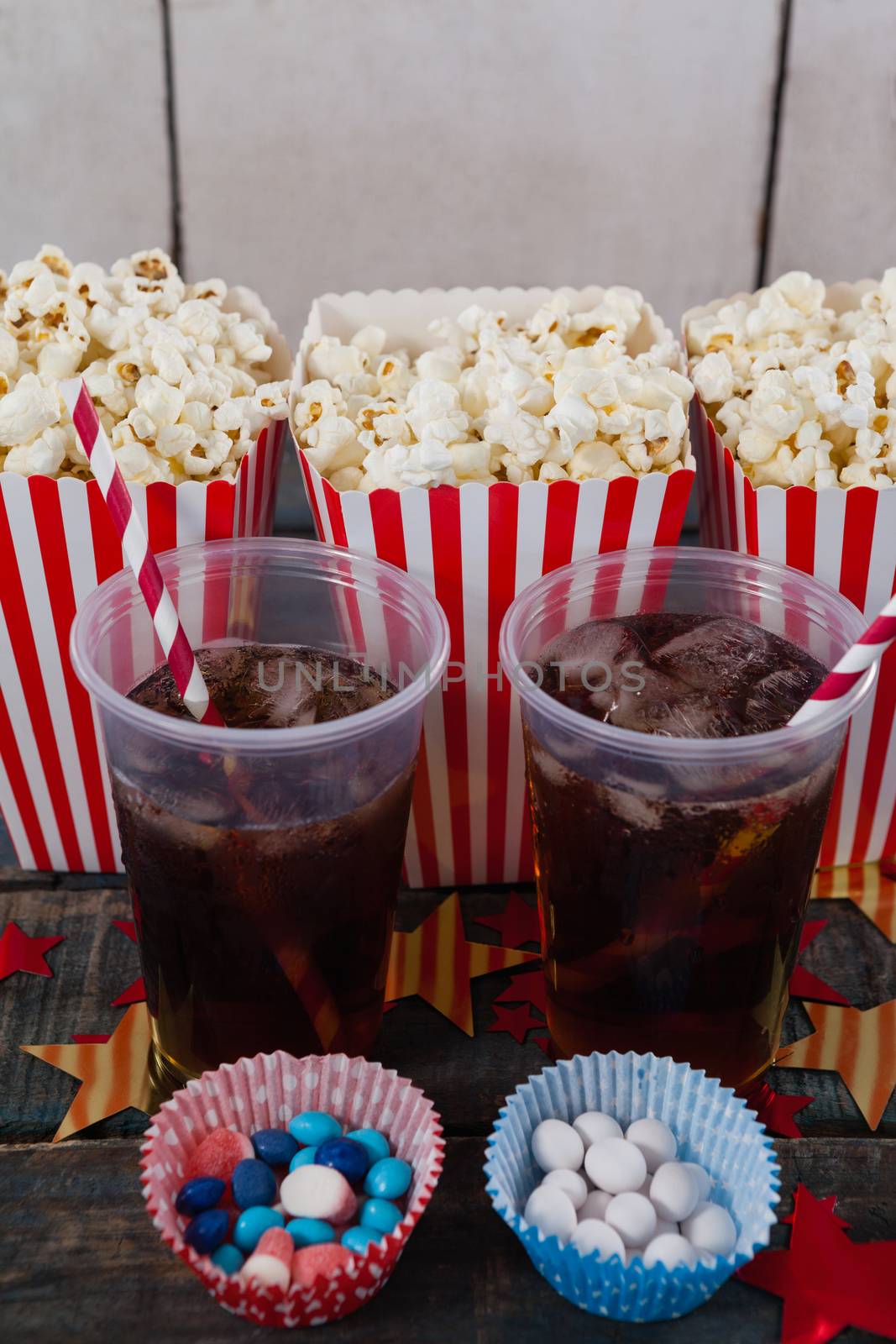 Popcorn, confectionery and drink on wooden table with 4th july theme