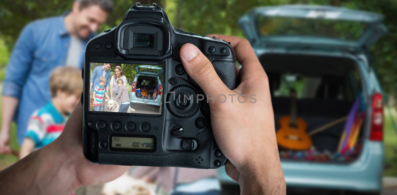 Cropped image of hands holding camera  against family with kids and pet dog at picnic