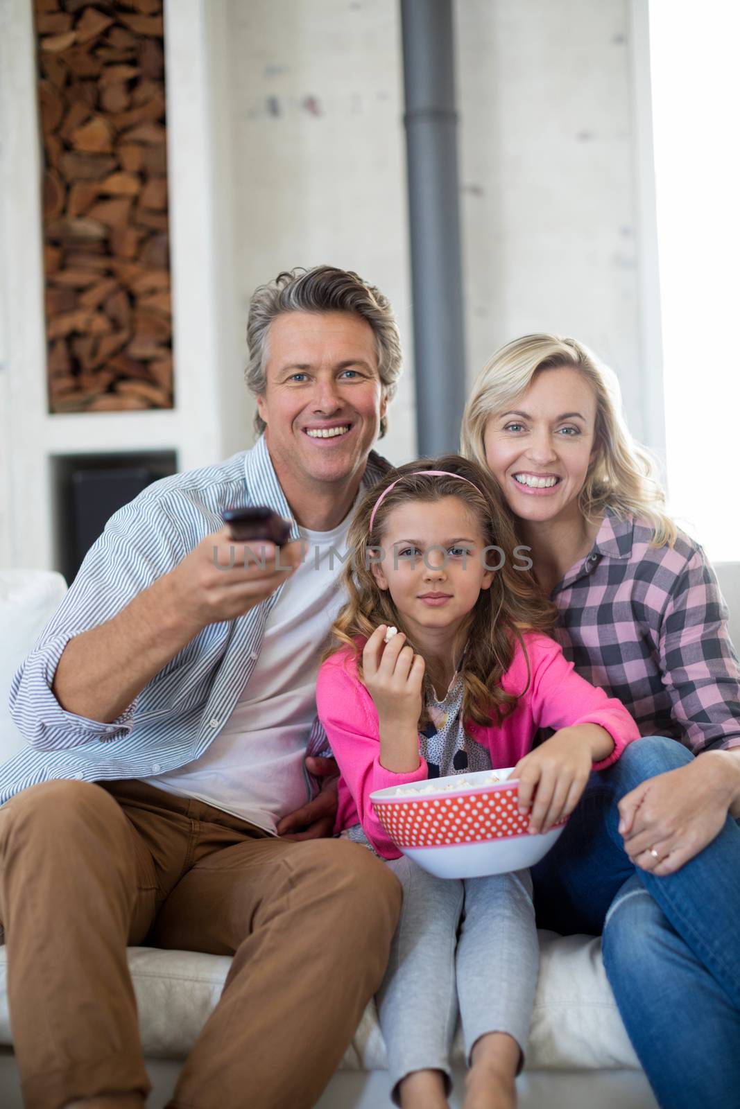 Smiling family watching television while having popcorn in living room at home