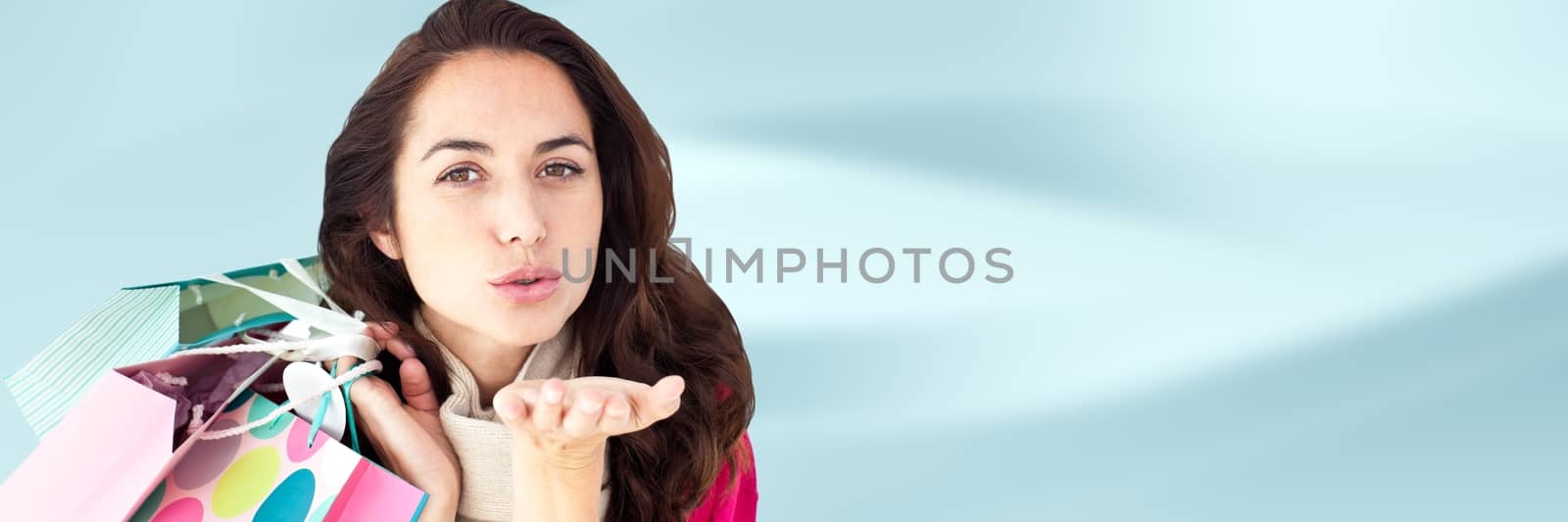 Digital composite of Shopper with bags and blowing kiss against blurry blue abstract background