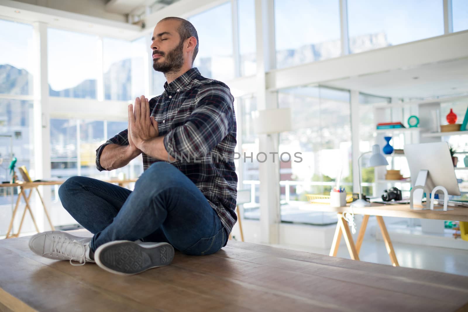 Male executive performing yoga on a table in the office