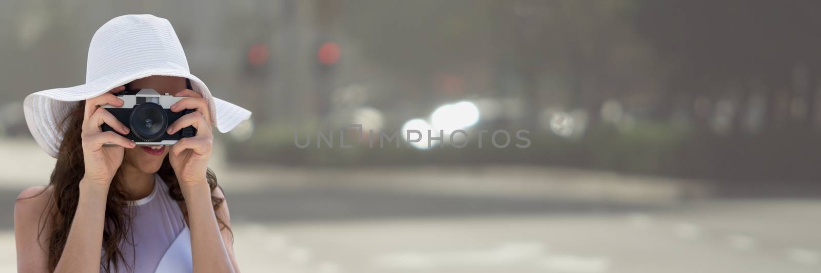 Millennial woman in summer hat with camera against blurry street by Wavebreakmedia
