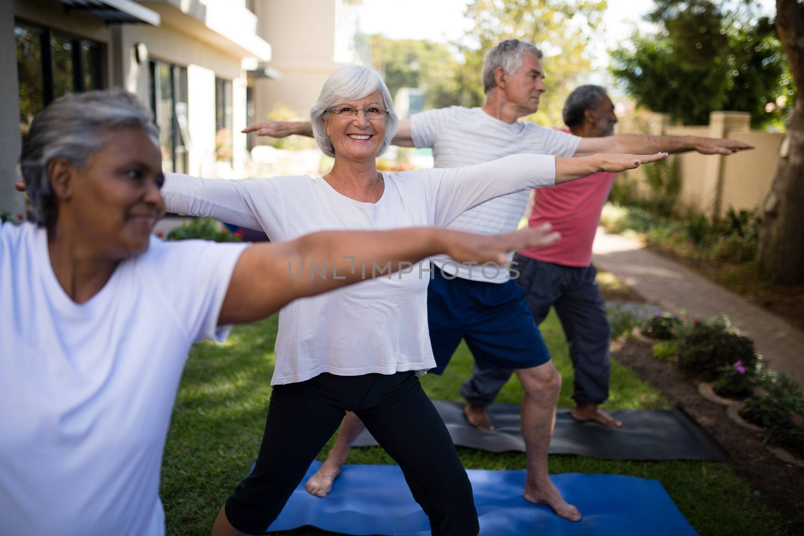 Smiling senior woman exercising with friends on yoga mats at park