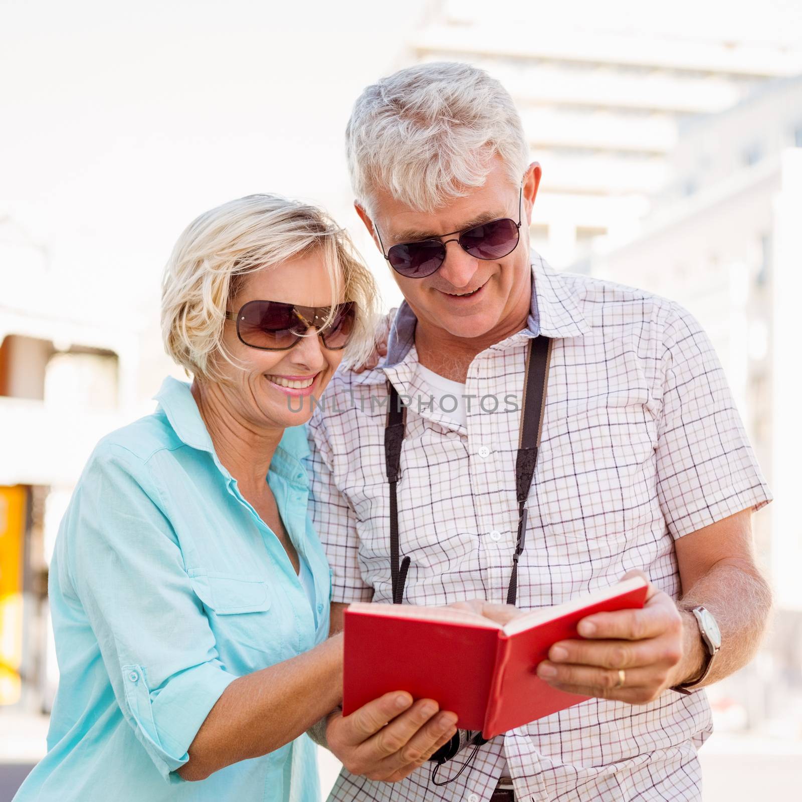 Happy tourist couple using tour guide book in the city by Wavebreakmedia