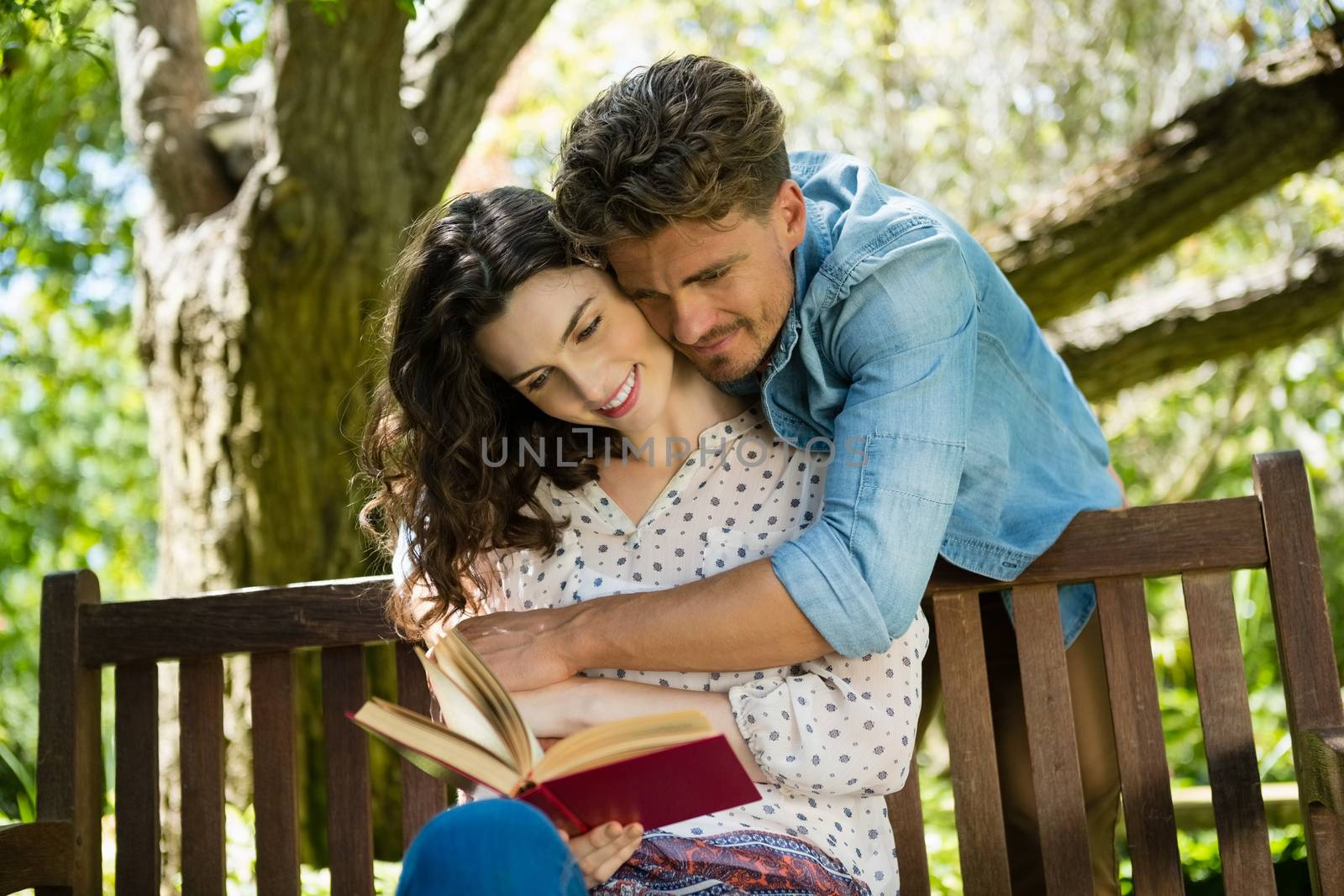 Romantic couple reading book on bench in garden by Wavebreakmedia