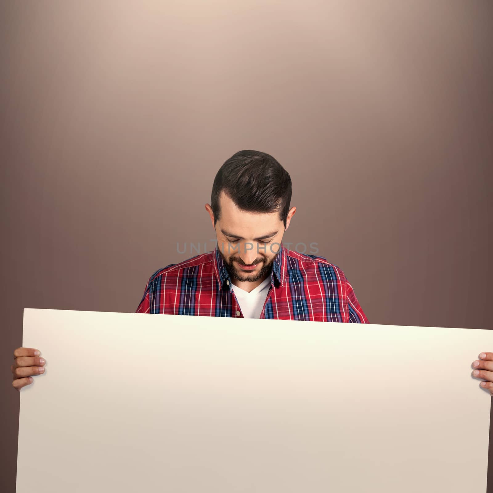 Young man holding blank placard against brown background