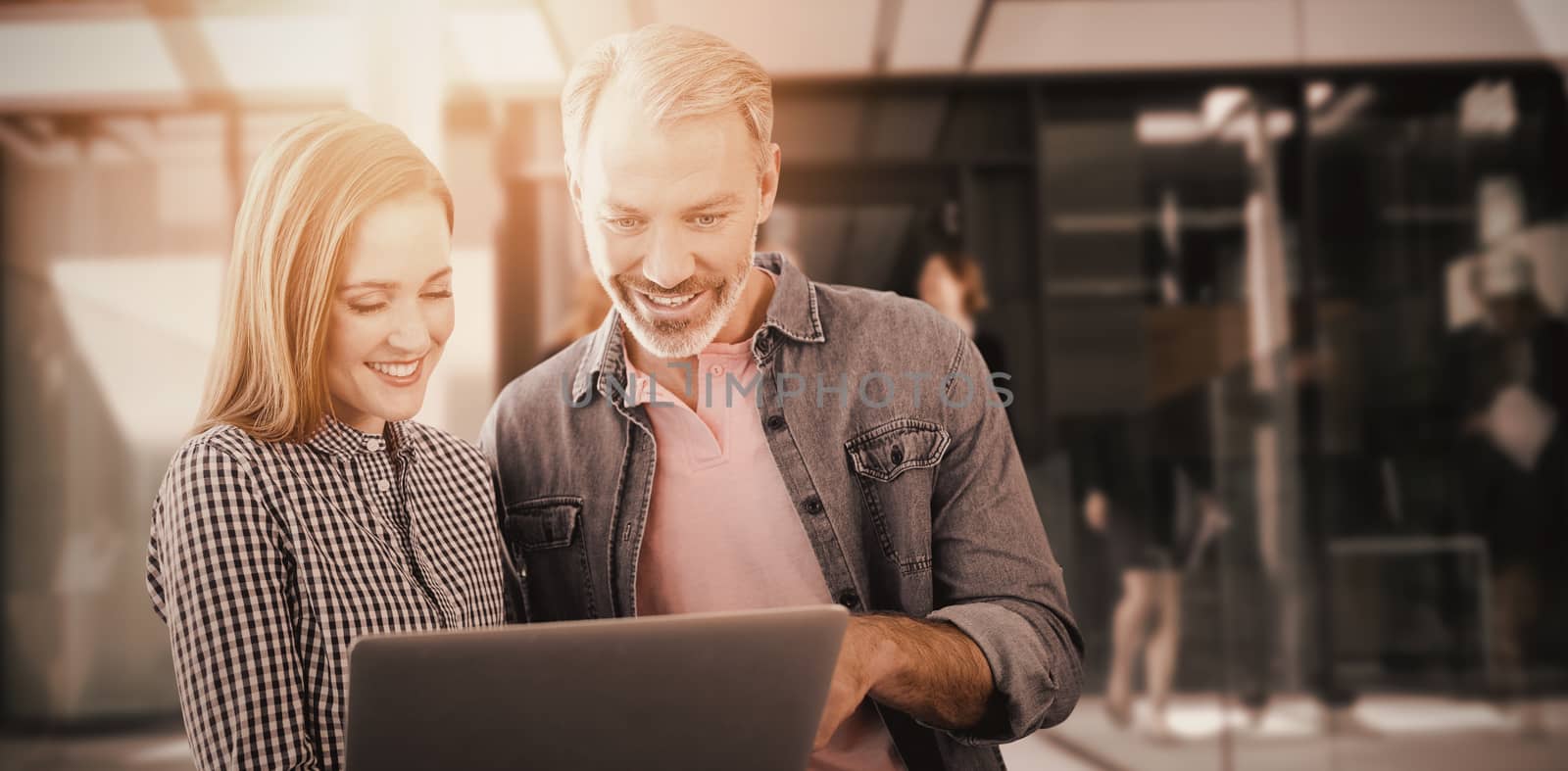 Portrait of smiling business people using laptop against businesspeople walking in the office