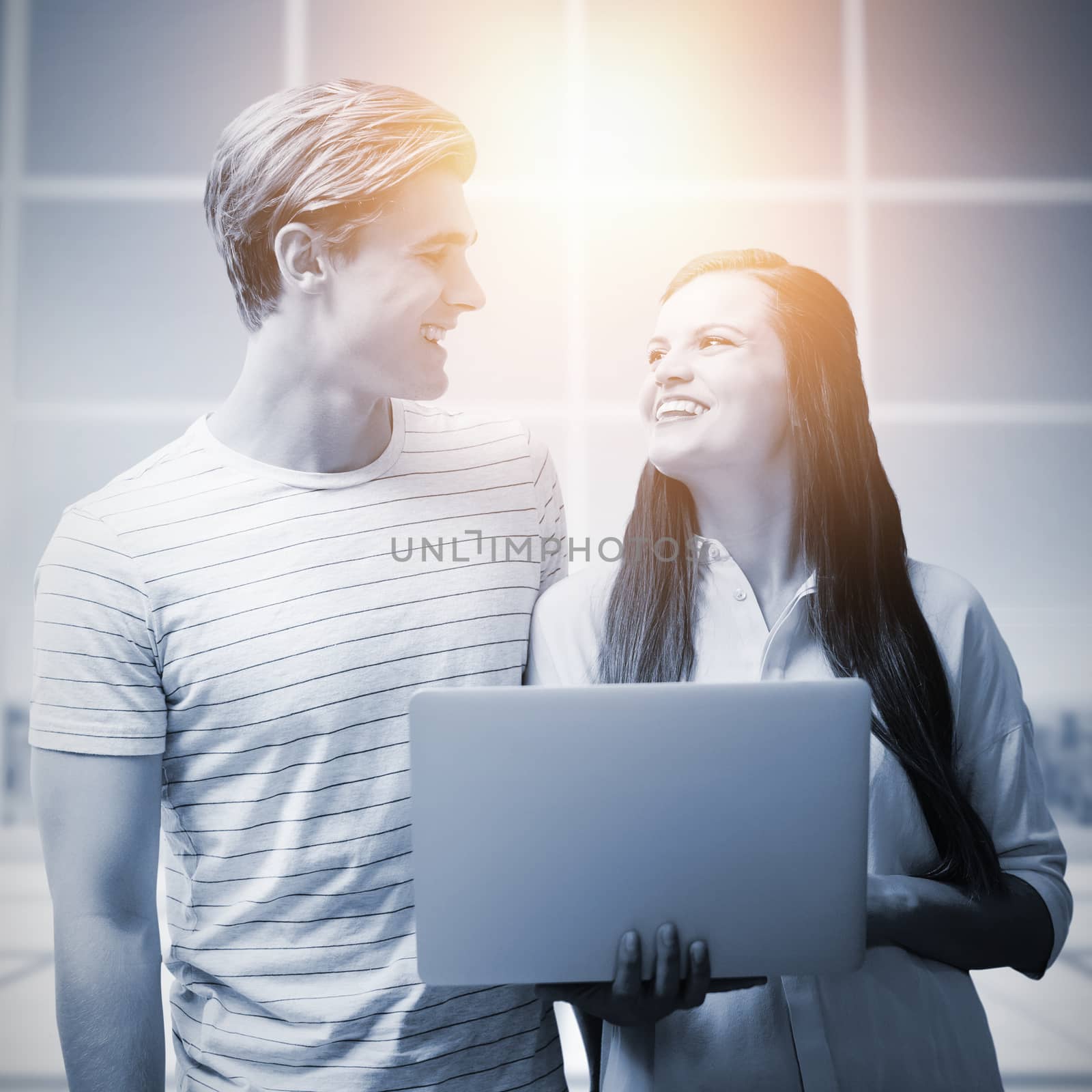 Composite image of smiling colleagues looking at each other while using laptop by Wavebreakmedia