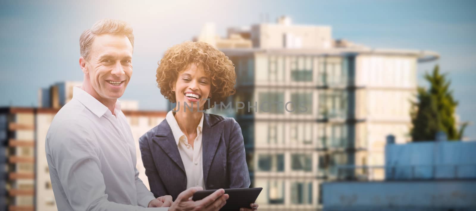 Portrait of business people posing with digital tablet  against sunlight falling on buildings against sky