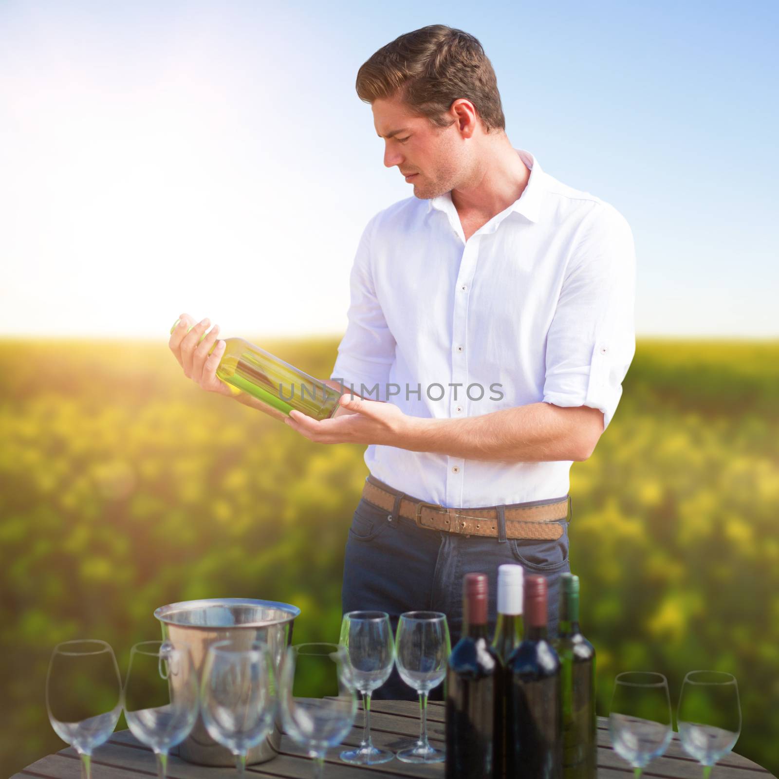 Young man holding wine bottle by glasses on barrel against scenic view of beautiful mustard field