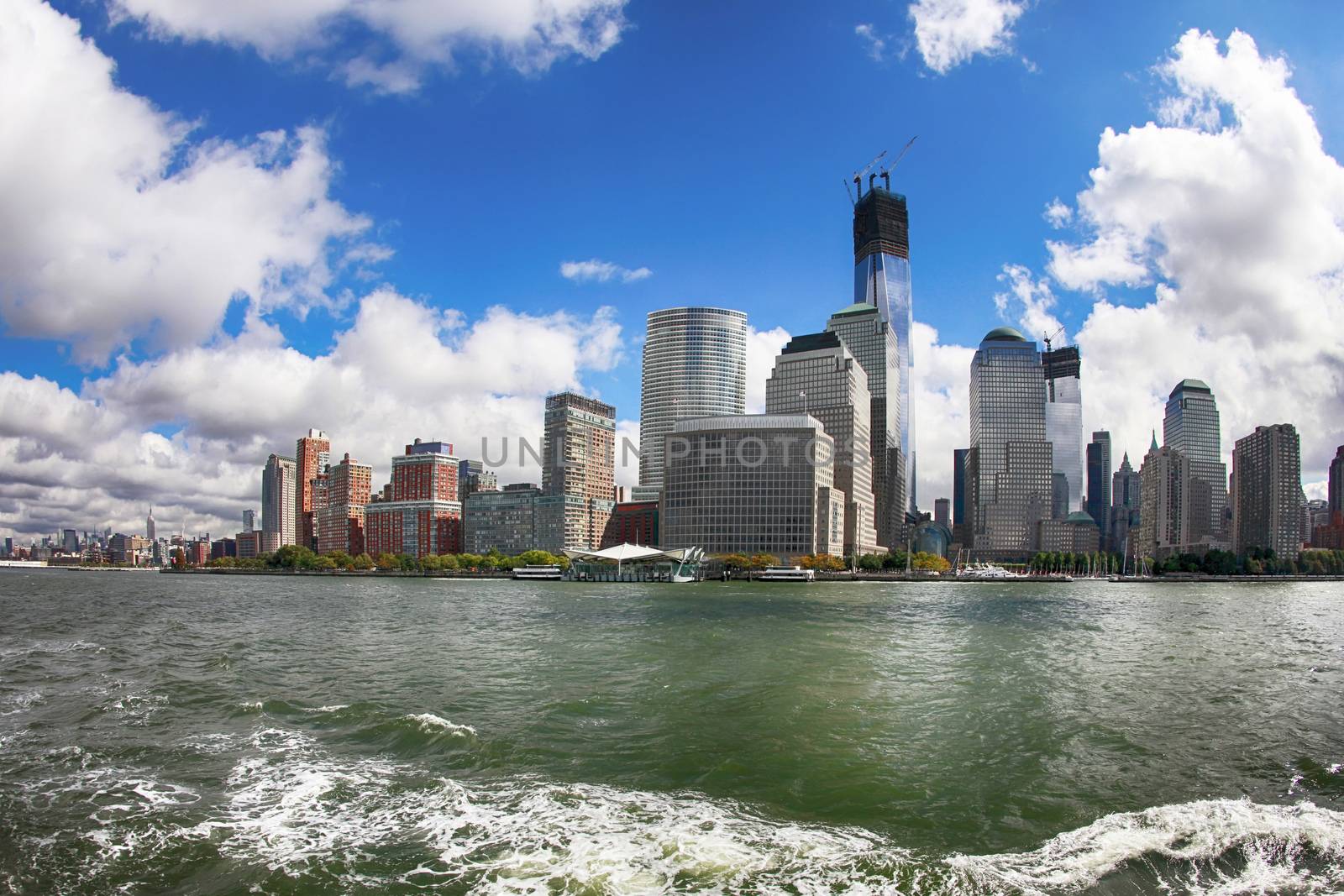 A shot from a ferry looking back at Manhattan skyline. The water shows trace left by the ferry boat. 