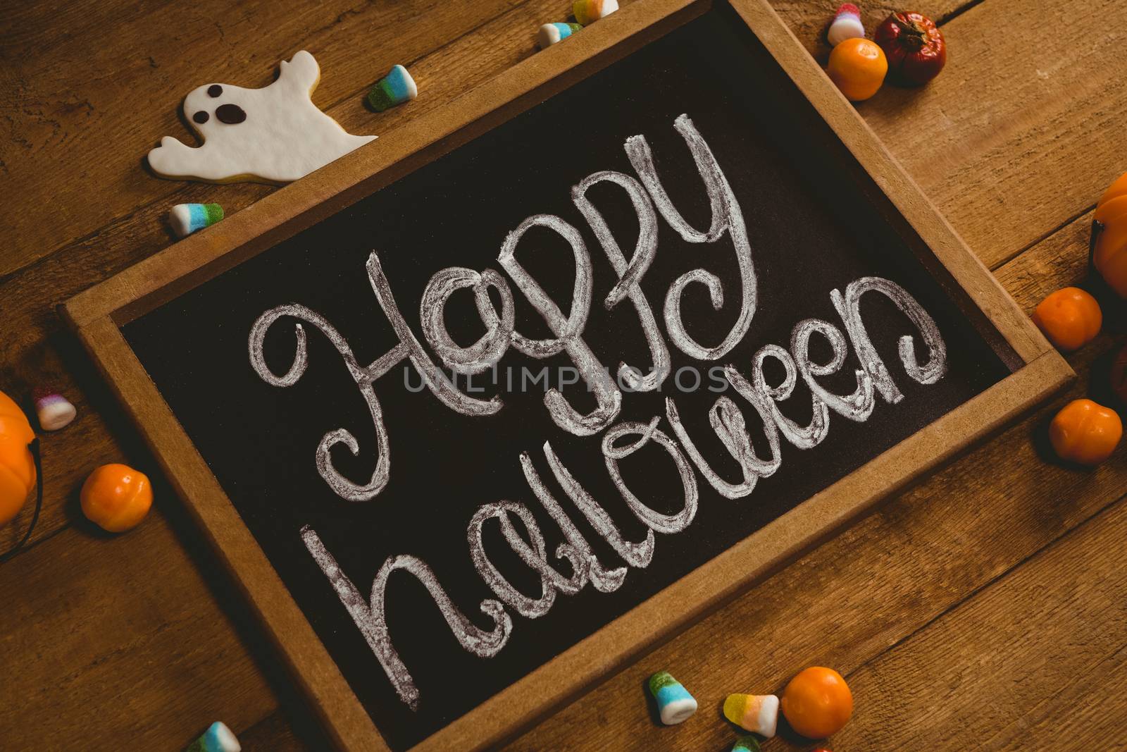 High angle view of slate with happy Halloween text by candies on wooden table