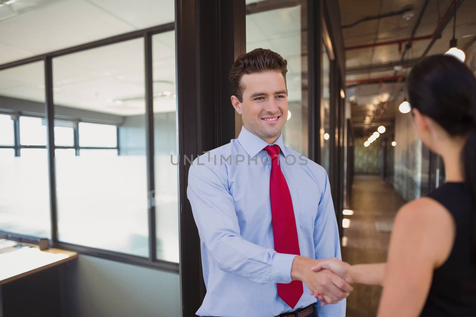 Happy business people shaking hands against office background by Wavebreakmedia