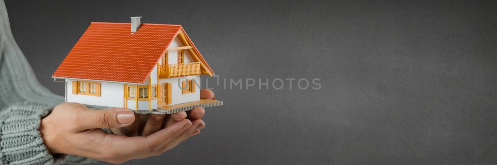 Woman holding a house against grey background as concept of insurance by Wavebreakmedia