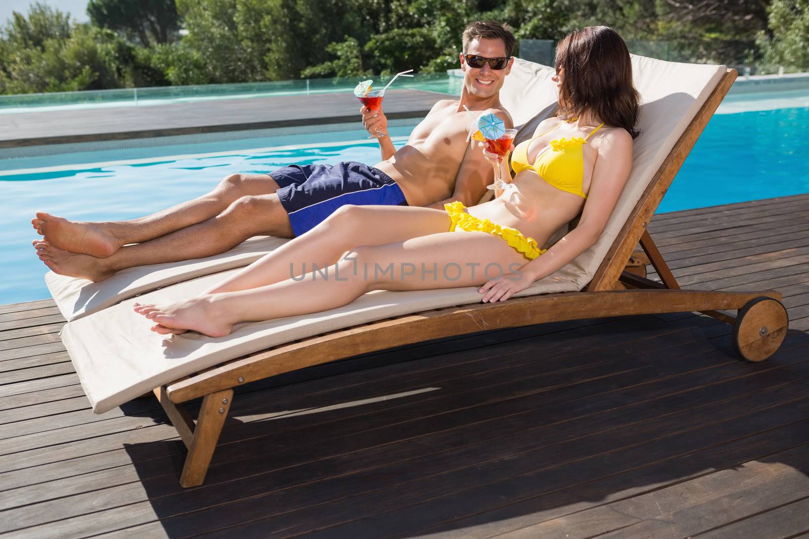 Couple with drinks sitting by swimming pool by Wavebreakmedia