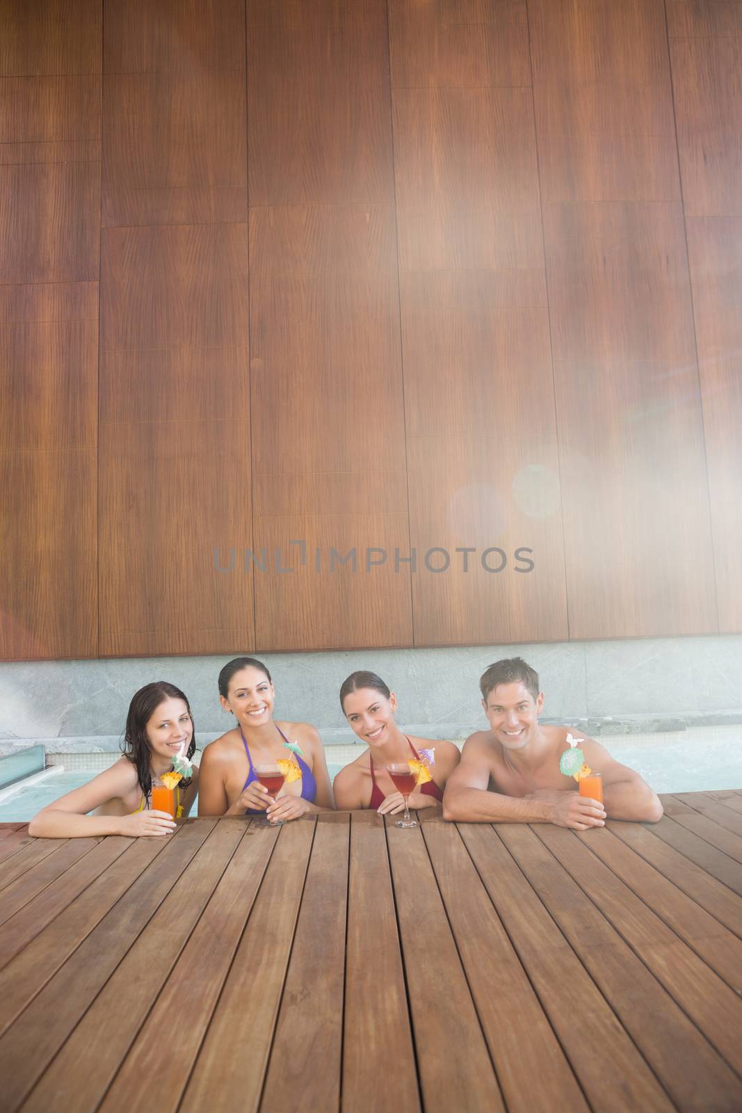 Portrait of cheerful young people with drinks in the swimming pool