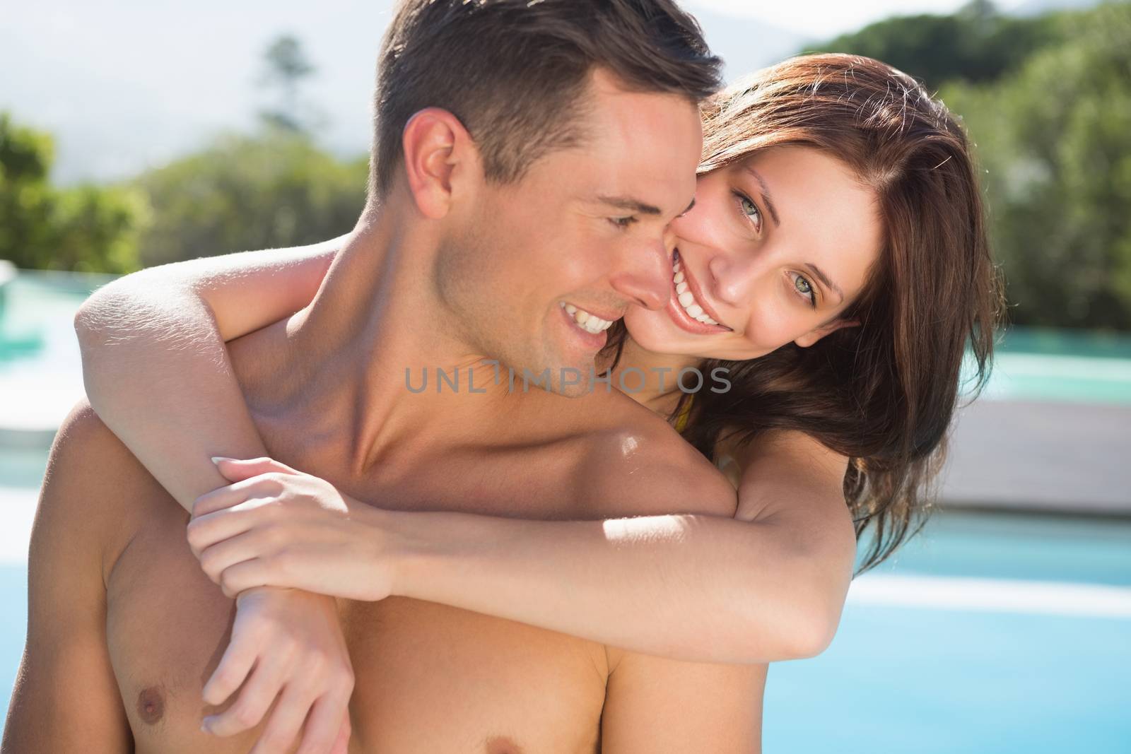 Portrait of a romantic young woman embracing man by swimming pool on a sunny day