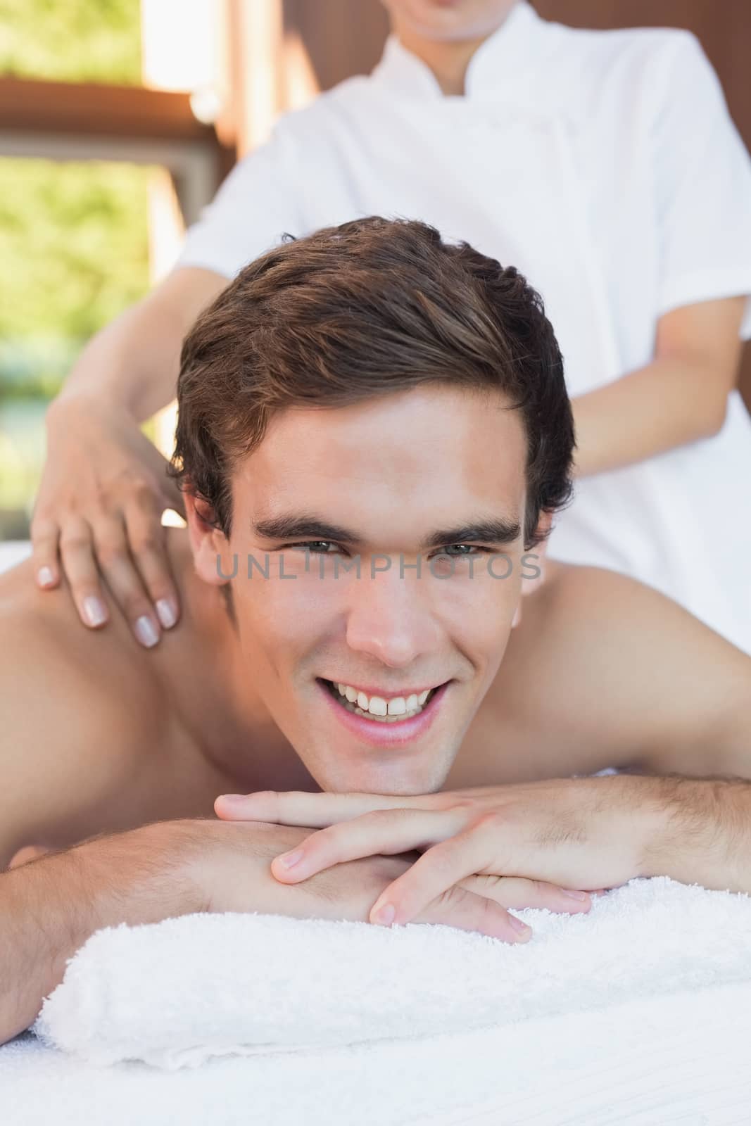 Close up of a handsome young man receiving shoulder massage at spa center