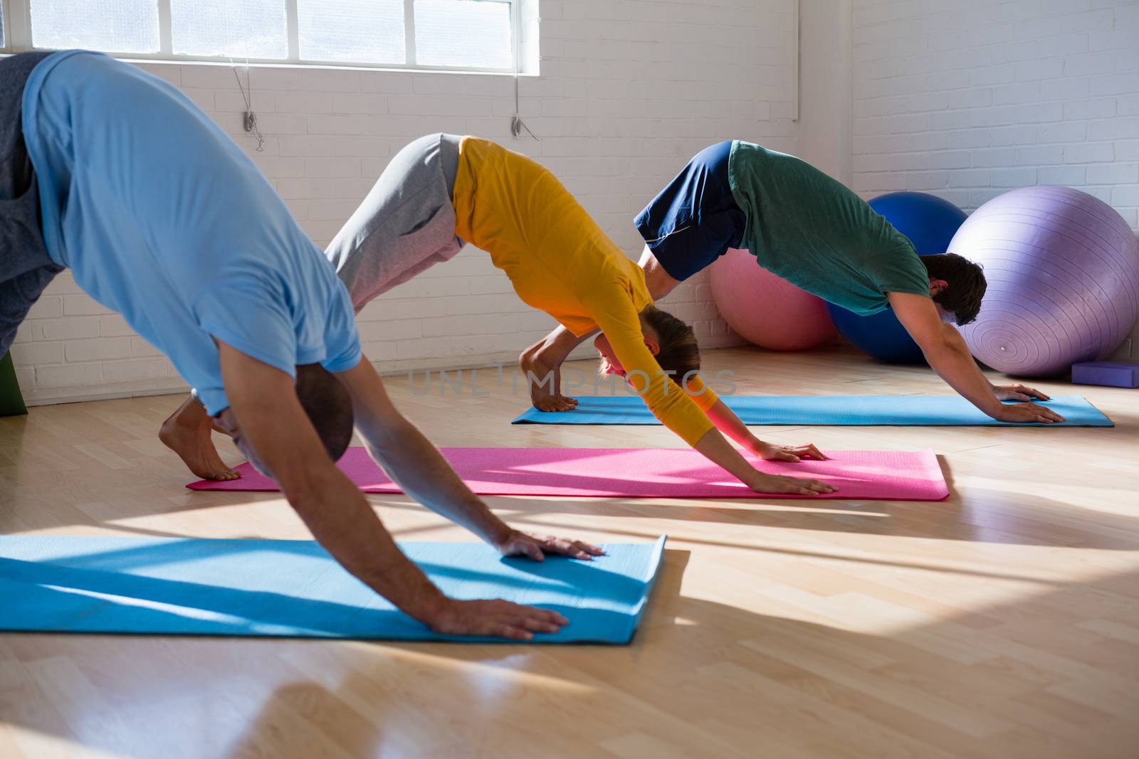 Instructor with students practicing downward facing dog pose in health club by Wavebreakmedia