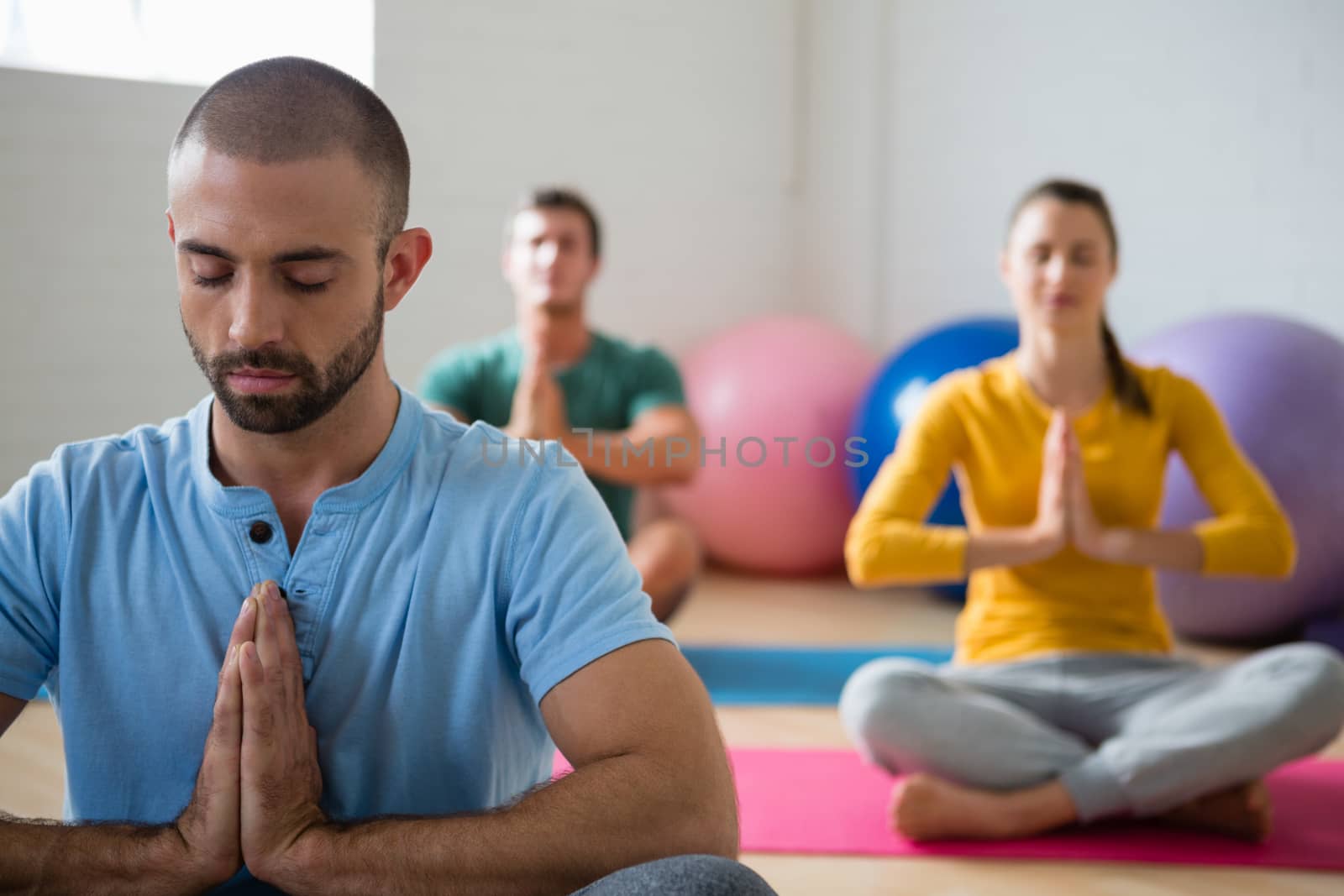 Yoga instructor with students meditating in prayer position at club  by Wavebreakmedia