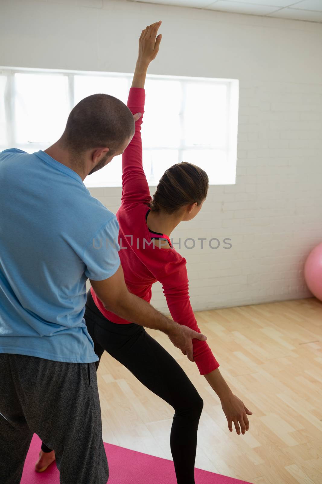 Rear view of yoga instructor assisting student in exercising at health club