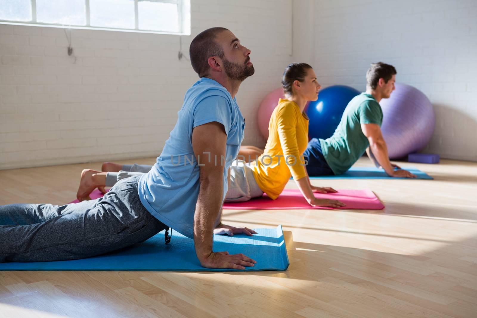 Male instructor with students practicing cobra pose in yoga studio