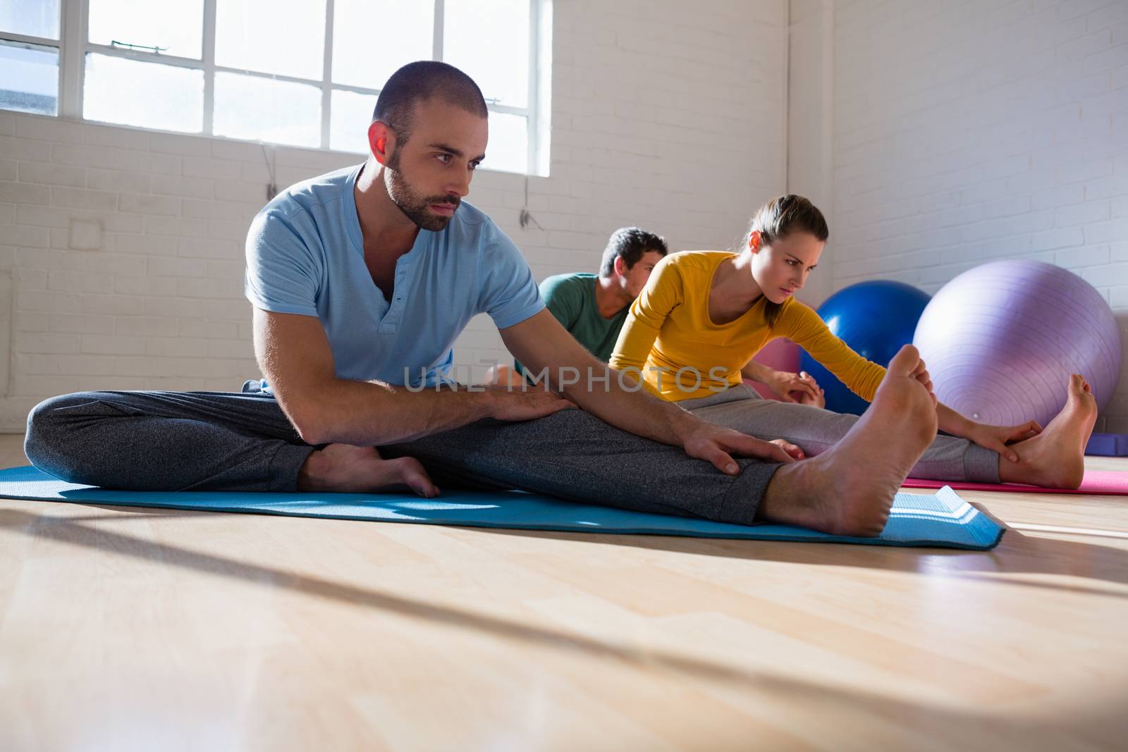 Yoga instructor with students stretching legs at health club