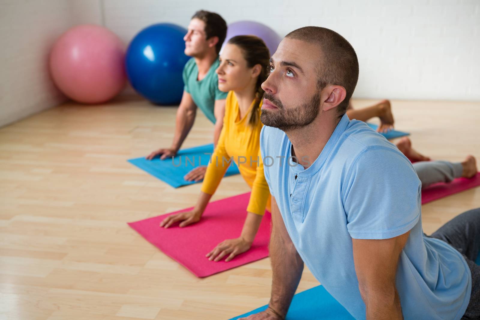 Male instructor guiding students in practicing cobra pose at yoga studio