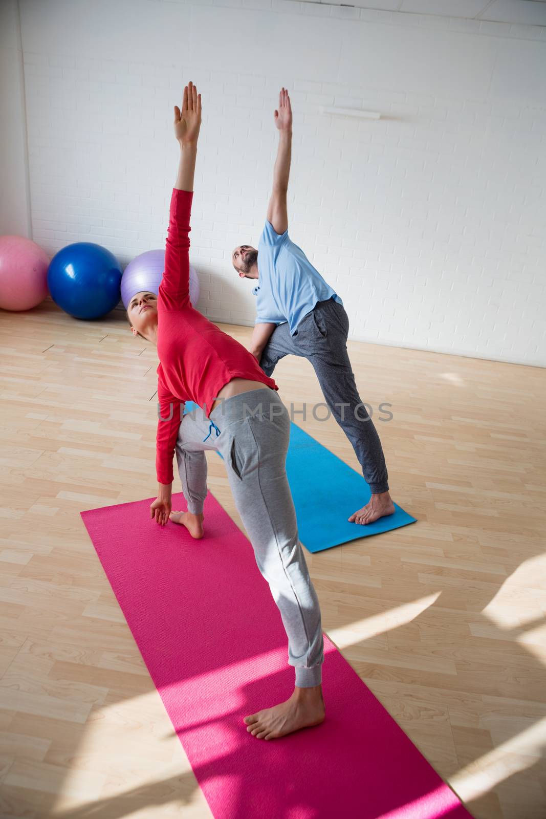 Instructor with female student practicing triange pose in yoga studio